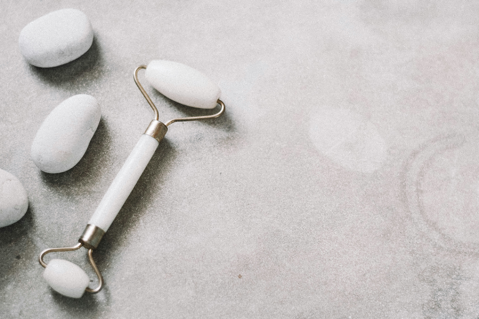 White jade roller and smooth massage stones on a soft marble surface